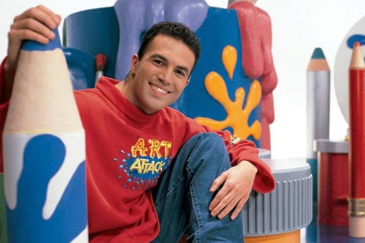 Presentador Rui Torres de Art Attack sonriendo en un set colorido con lápices gigantes.