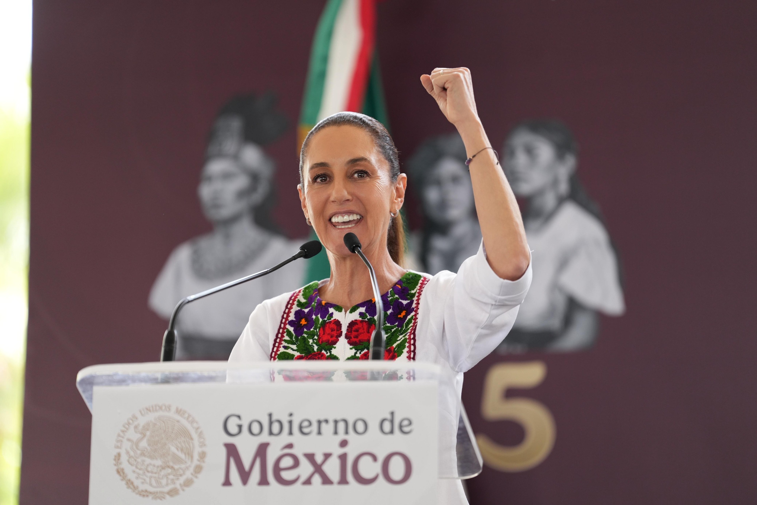 Claudia Sheinbaum hablando en un podio del Gobierno de México levantando el puño.