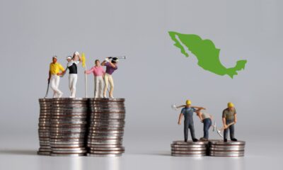 Monedas y billetes junto a una casa y un auto en miniatura, con una calculadora y documentos financieros, simbolizando economía familiar y lucha económica.