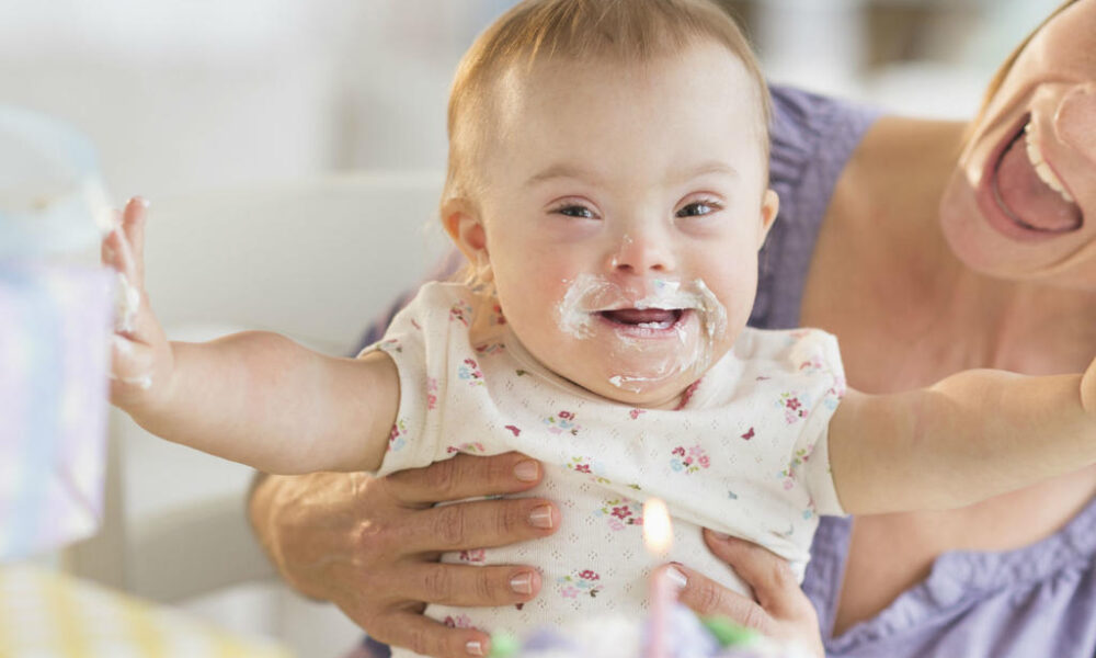 Bebé sonriente con pastel en el rostro mientras una persona adulta la sostiene durante una celebración.