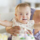 Bebé sonriente con pastel en el rostro mientras una persona adulta la sostiene durante una celebración.