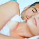 Pareja joven dormida abrazada en una cama mientras descansan.