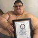 Juan Pedro Franco, ex hombre más obeso del mundo, sostiene un certificado Guinness mientras está sentado en una cama.