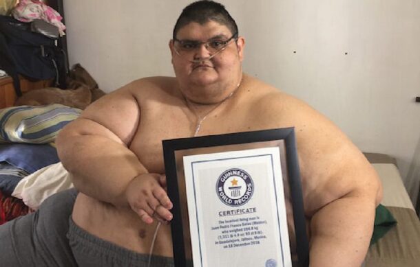 Juan Pedro Franco, ex hombre más obeso del mundo, sostiene un certificado Guinness mientras está sentado en una cama.