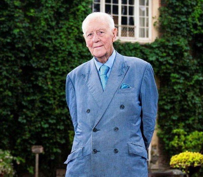 Sir Benjamin Slade, multimillonario británico de 79 años, posando frente a su mansión y un auto de lujo.