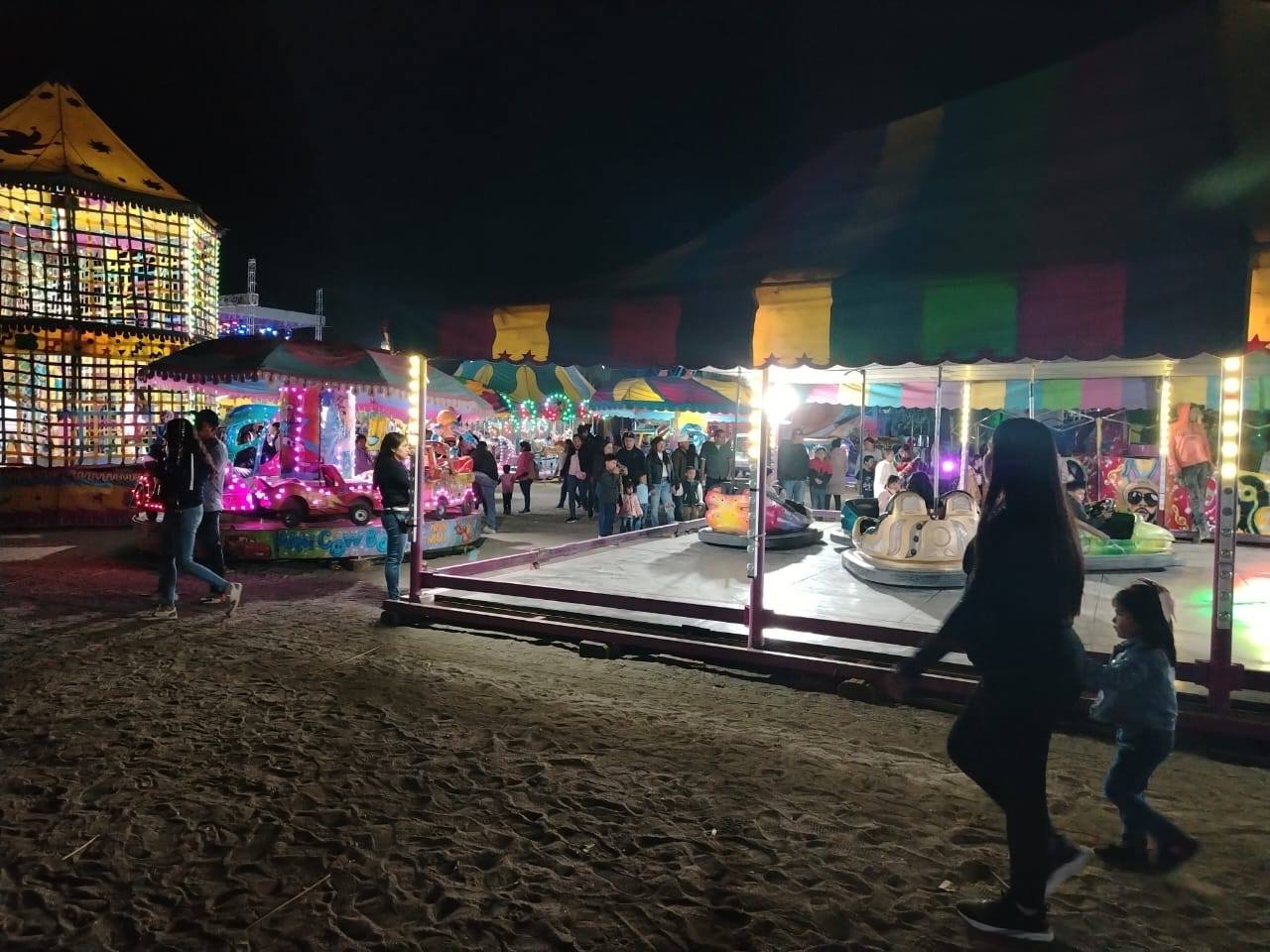 Feria nocturna en fiesta patronal con juegos mecánicos y familias recorriendo el área en Tezonteopan de Bonilla.