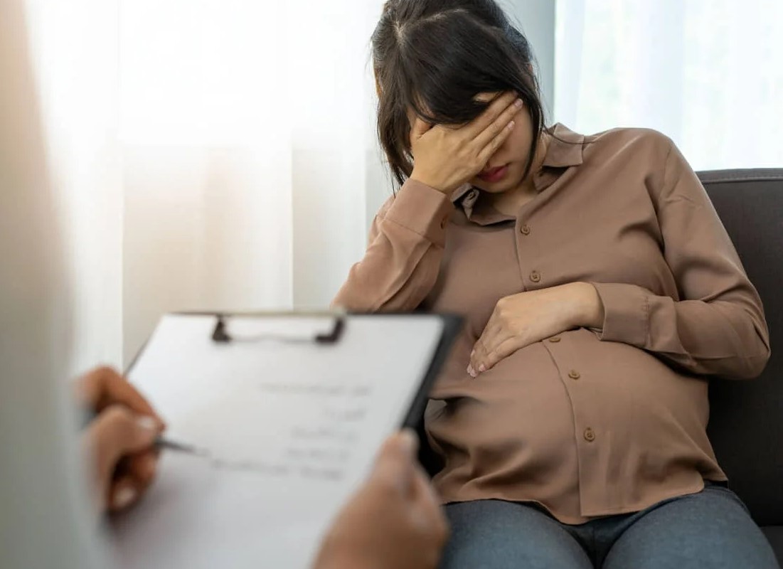 Mujer embarazada con expresión de angustia durante consulta médica.