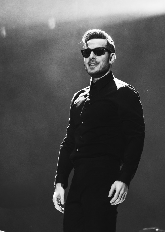 “José Madero cantando en concierto, vestido de negro y sosteniendo un micrófono, durante su presentación en un estadio iluminado.”