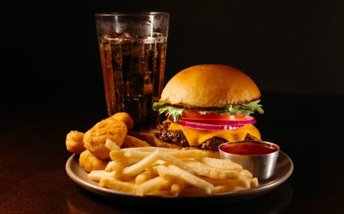 "Plato con hamburguesa, papas fritas, nuggets y refresco, representando alimentos ultraprocesados asociados al adelanto de la menstruación."