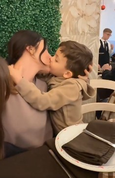 Madre expresa afecto a su hijo con un beso en la boca durante una convivencia familiar.
