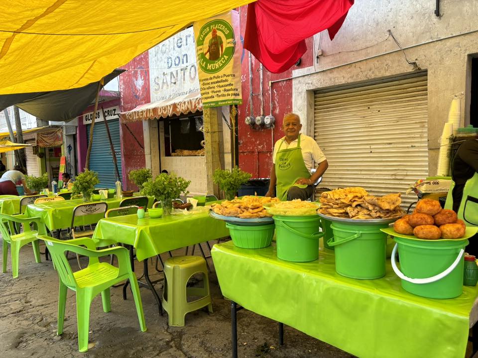 Puesto callejero de tacos con mesas verdes y alimentos expuestos en la vía pública.
