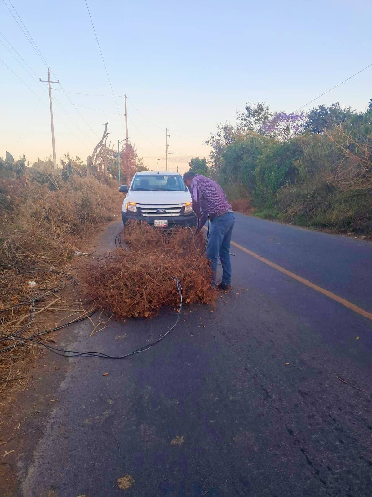 Personal de Servicios Públicos del Ayuntamiento de Tochimilco realiza reacomodo de cables sobre vialidad cercana a una escuela para prevenir riesgos tras rachas de viento.