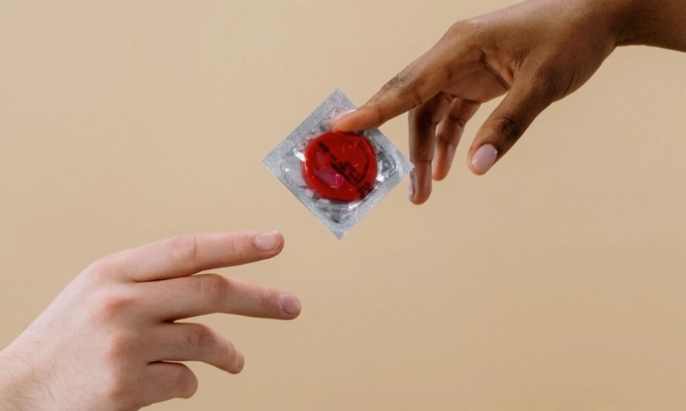 Manos intercambiando un condón empaquetado, símbolo de prevención y salud sexual.