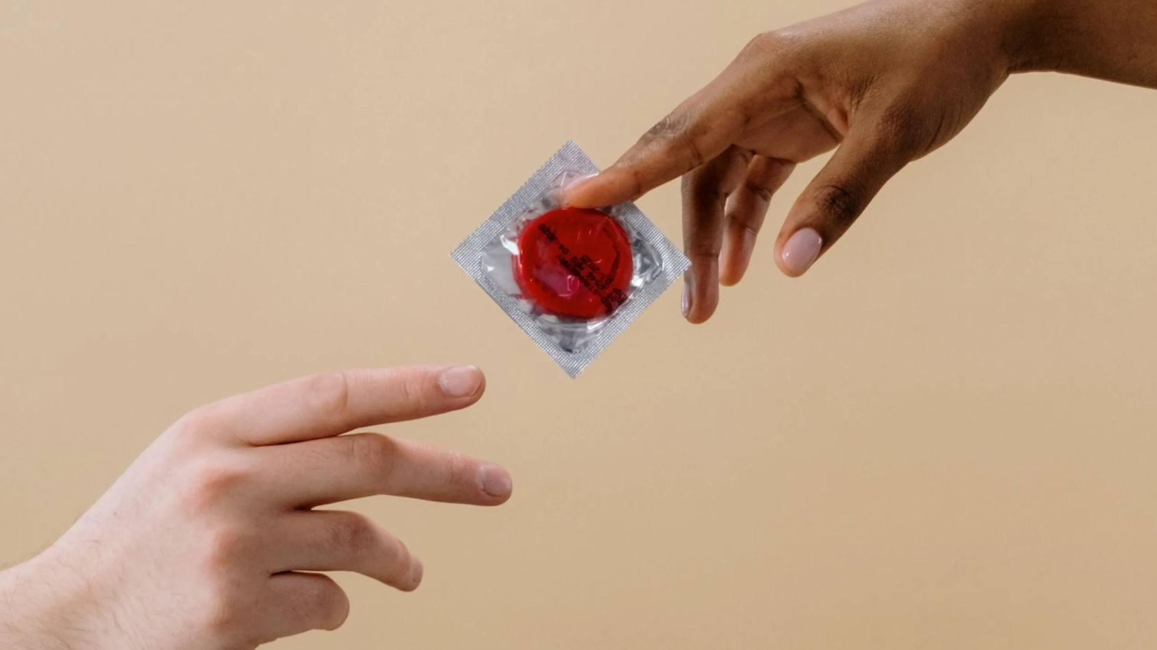 Manos intercambiando un condón empaquetado, símbolo de prevención y salud sexual.
