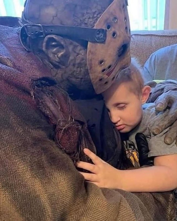 Cosplayer de Jason Voorhees acompañando de forma afectuosa a un niño pequeño, en un momento de consuelo emocional.