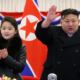 Líder de Corea del Norte acompañado de una menor en evento oficial frente a bandera nacional.