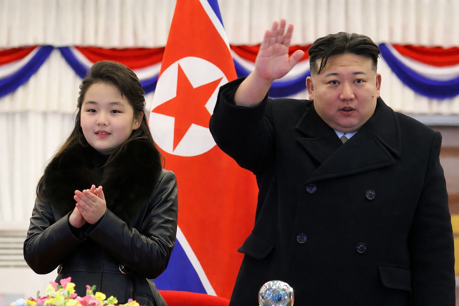 Líder de Corea del Norte acompañado de una menor en evento oficial frente a bandera nacional.