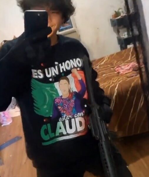 Joven frente a espejo usando camiseta con mensaje político, sosteniendo un objeto con apariencia de arma larga.