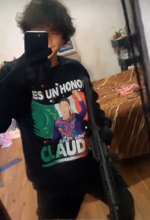 Joven frente a espejo usando camiseta con mensaje político, sosteniendo un objeto con apariencia de arma larga.