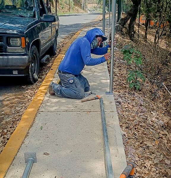 Trabajador instalando malla ciclónica en vialidad de Tochimilco para proteger a estudiantes cerca de barranca