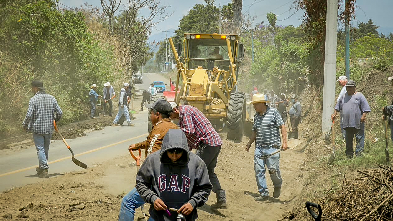 Faena comunitaria en Tochimilco con maquinaria y ciudadanos limpiando cunetas en la entrada principal del municipio