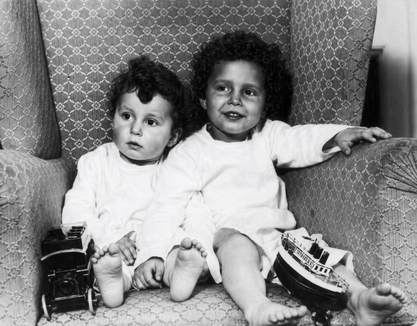 Fotografía en blanco y negro de dos niños sobrevivientes del Titanic sentados en un sillón con juguetes.