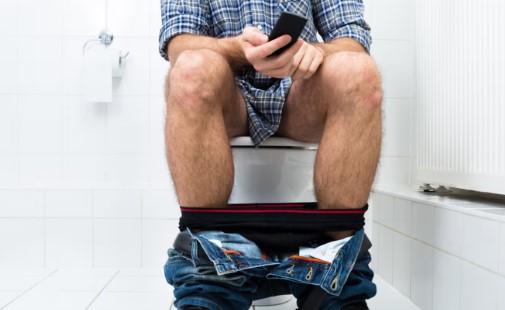Persona usando celular mientras está sentada en el baño, relacionado con hábitos de salud