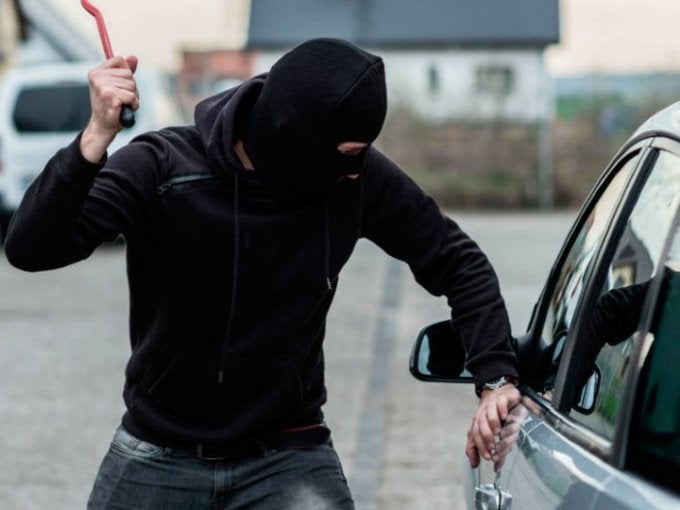 Persona intentando forzar la puerta de un automóvil, representando riesgos de inseguridad en vía pública