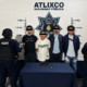 # Texto ALT Cuatro hombres detenidos por elementos de la Secretaría de Seguridad Pública de Atlixco tras una persecución en la colonia Álvaro Obregón. En la mesa de indicios se observa un arma corta, cartuchos útiles y un cargador asegurados durante el operativo. --- # Título de la imagen Detienen a cuatro hombres en Atlixco; aseguran arma de fuego tras persecución --- # Leyenda Elementos de la Secretaría de Seguridad Pública de Atlixco presentaron a cuatro hombres detenidos luego de una persecución derivada de un reporte ciudadano. Durante el operativo fue asegurada un arma corta abastecida, cartuchos útiles y un cargador, los cuales quedaron a disposición de la autoridad competente para las investigaciones correspondientes. --- # Descripción Fotografía oficial de la **Secretaría de Seguridad Pública de Atlixco** en la que aparecen **cuatro hombres detenidos** tras una persecución registrada en la colonia **Álvaro Obregón**, en el municipio de Atlixco, Puebla. La intervención policial inició luego de que una ciudadana reportó un **vehículo Mazda color rojo** que circulaba con las luces apagadas y cuyos ocupantes presuntamente realizaron detonaciones de arma de fuego al aire. Tras un operativo de búsqueda, elementos municipales interceptaron la unidad sobre la **calle 9 Poniente número 113**. Durante la inspección del vehículo, los oficiales localizaron un **cartucho percutido** y posteriormente aseguraron un **arma corta abastecida con cartuchos útiles**, la cual se encontraba debajo del asiento del conductor. En la imagen también se aprecia el armamento asegurado colocado sobre una mesa de indicios, acompañado por el cargador y la munición correspondiente. Los cuatro detenidos fueron puestos a disposición de la autoridad competente, que será la encargada de determinar su situación jurídica conforme al debido proceso. Es importante señalar que, de acuerdo con la legislación mexicana, toda persona detenida goza del derecho a la **presunción de inocencia** hasta que exista una resolución judicial firme. La imagen ilustra una acción de seguridad pública derivada de la atención a un reporte ciudadano y sirve como apoyo visual para informar sobre los resultados del operativo realizado por la Policía Municipal de Atlixco, así como para destacar la importancia de la denuncia oportuna en la prevención y combate de hechos delictivos.