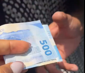 Turista muestra un billete mientras denuncia un presunto cobro excesivo de un taxista.