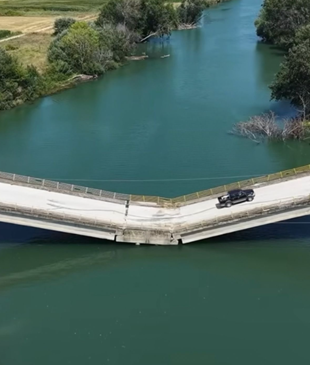 Puente con aparente colapso estructural por el que continúa circulando un vehículo.